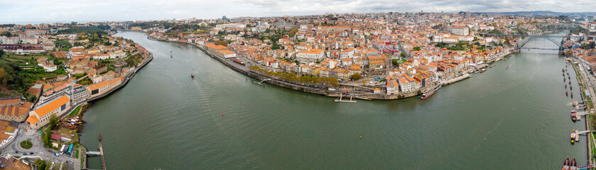 Fototapeta na wymiar Panoramic aerial view of Porto city. View of Douro River. At right is Dom Luis I Bridge, at left Ponte da Arrabida. Panoramic perspective of old town center. Cloudy day. Famous travel destination. 