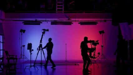 Professional filming pavilion with a neon cyclorama. The process of preparing for the shooting of a music video. Director, Cameraman and crew in Backstage.