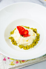 curd dessert with strawberries on top in a white plate on a marble background, side view
