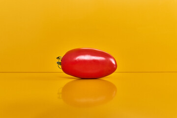 Tomate rouge italienne entière posée sur fond jaune vue de face avec reflet