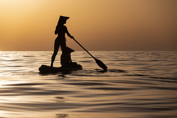 a woman with a child on a sup board in the sea swim against the background of a beautiful sunset,...