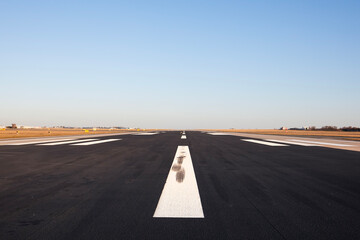 Surface level of long airport runway with directional marking against clear sky. .