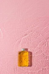 Vertical image of beauty product bottle in water with copy space background on pink background