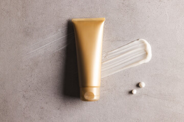 Beauty product gold tube and cream smudges with copy space on stone background