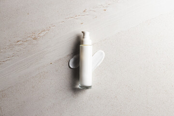 Beauty product bottle with pump and cream smudges with copy space on stone background