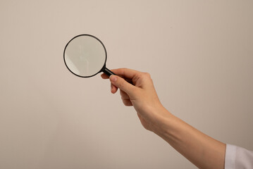 Woman holding magnifying glass on grey background, closeup. Find keywords concept