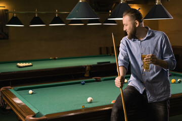 Billiard sport concept. Attractive man drinking beer near billiards table
