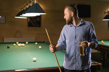 Handsome young caucasian man drinking beer beside billiard table in bar