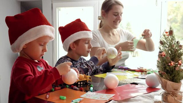 Happy kids with mother cutting out Christmas garlands from colorful paper. Winter holidays, family time together, kids with parents celebrating