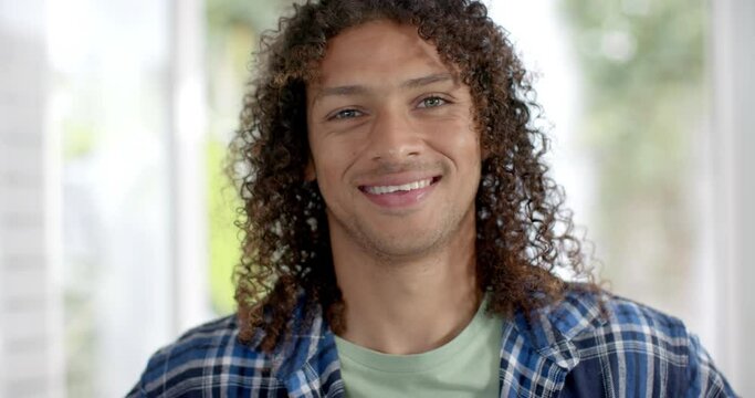Portrait of happy biracial man with long curly dark hair smiling at home, slow motion