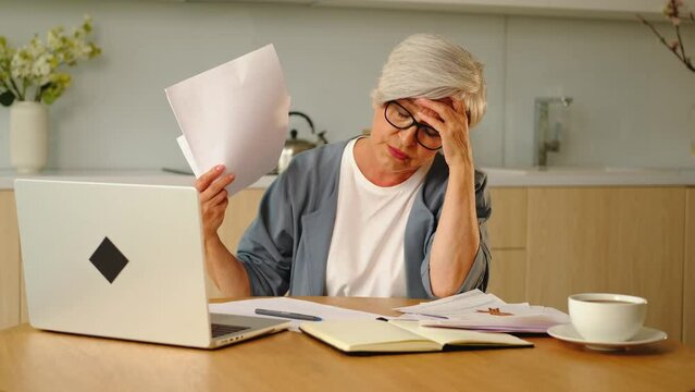 Sad tired disappointed older senior woman with paper document and laptop. Unhappy mature grandmother experiencing stress managing bank finances calculating taxes planning loan debt pension payment