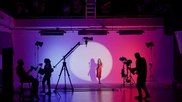 Professional filming pavilion with a neon cyclorama. The process of preparing for the shooting of a music video. Director, Cameraman and crew in Backstage.