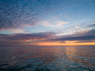 A view from a drone flying over the sea early in the morning at sunrise, with the rising sun and a colorful sky