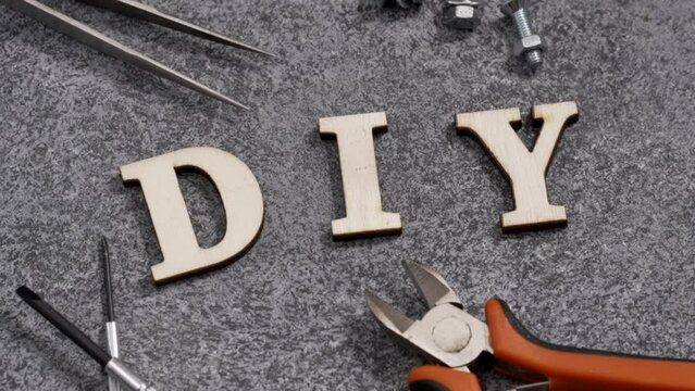 DIY, do it yourself, spelled in wooden letters and animated with stop motion. Various tools and fasteners around.