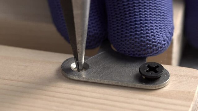 A carpenter marks and drill hole in the board for a self-tapping screw to attach a furniture keyhole hanger, close-up