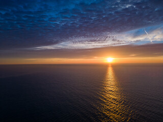 A view from a drone flying over the sea early in the morning at sunrise, with the rising sun and a colorful sky