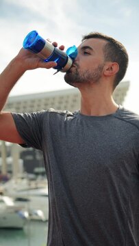 Vertical. Young handsome sportsman drinking energy water from bottle while resting after run workout. Male person of strong complexion having a break with a supplement and refreshing during training