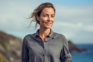 Portrait of a tender woman in her 30s sporting a breathable hiking shirt against a tranquil ocean...