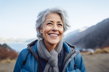 Portrait of a grinning woman in her 60s sporting a rugged denim jacket against a snowy mountain range. AI Generation - Powered by Adobe