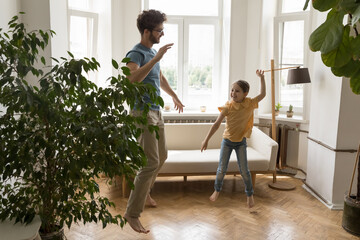 Active young father spend leisure time with cute child girl in apartment, dance in cozy living...