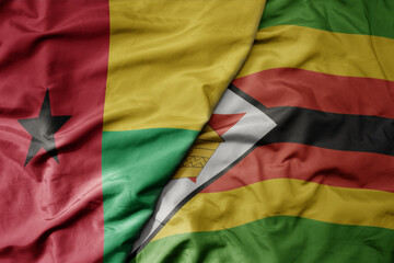 big waving national colorful flag of zimbabwe and national flag of guinea bissau .