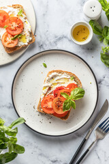Sandwich or toast with tomatoes, cream cheese, olive oil and basil on a plate on white marble background top view. Traditional mediterranean food
