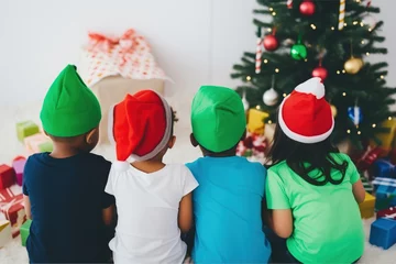 Foto op Plexiglas Rear view of four siblings of different races sharing excitement and enthusiasm as they explore the gifts under the tree on the magical Christmas Day. © SnapVault