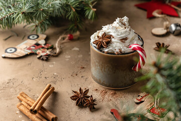 Hot cocoa with whipped cream and candy cane on festive brown table decorated with fir branches....