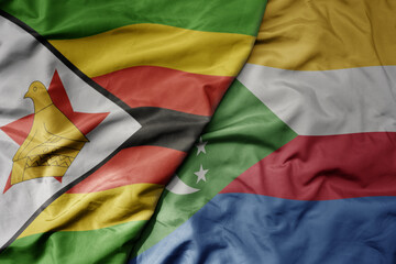 big waving national colorful flag of comoros and national flag of zimbabwe .