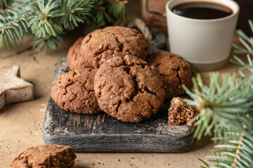 Homemade christmas chocolate cookies on wooden board and coffee on brown festive background with fir tree branches. Christmas holiday desserts