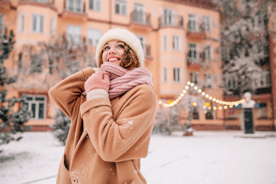Girl posing amid a city park and Christmas lights. Joyful woman stands in a snow-covered field during a snowfall.