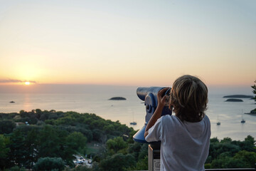  Boy looking through binocular at the islands in the sea during sunset, Vrsar, Croatia