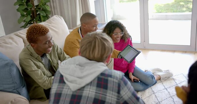 Happy diverse group of teenage friends using tablet and talking at home, slow motion
