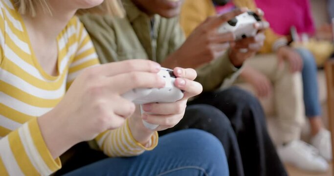Happy diverse group of teenage friends sitting on couch and playing video games at home, slow motion