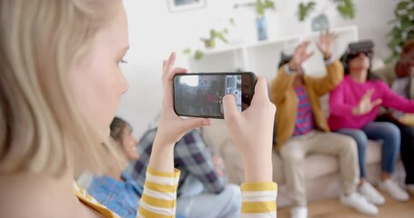 Diverse group of teenage friends recording with smartphone using vr headsets at home, slow motion