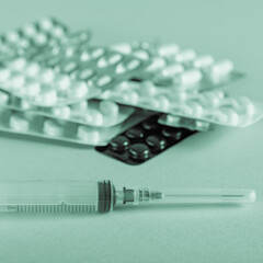 Different blisters of pills with disposable syringe in monochrome with green tinting