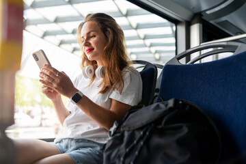 Young woman sits on the bus and uses her smart phone. Public city transportation and passenger. - obrazy, fototapety, plakaty