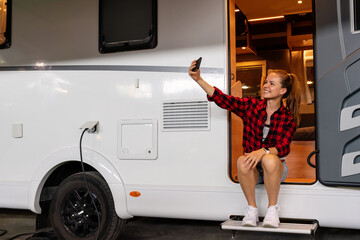 Young woman taking self portrait while sitting in the doorway of recreational vehicle camper van....