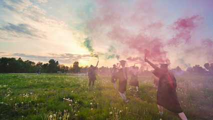 Graduates in costume walk with a smoky multi-colored smoke at sunset