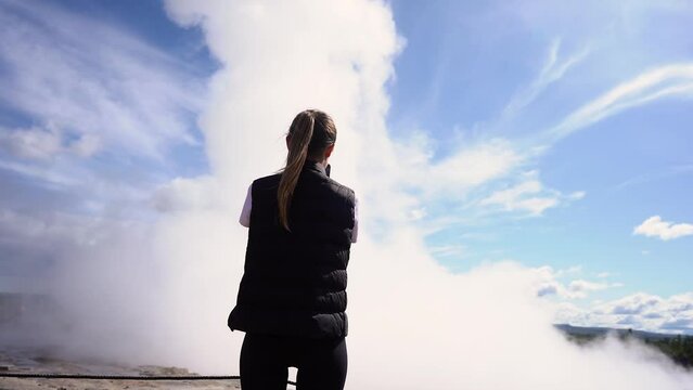 The tourist girl looks at the geyser in Iceland