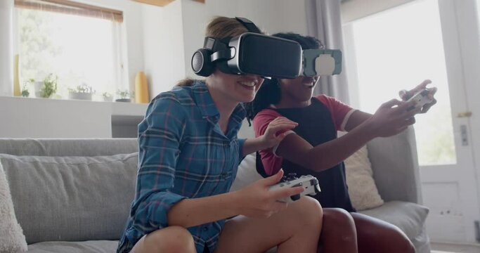 Happy diverse teenage female friends playing video games with vr headsets at home, slow motion