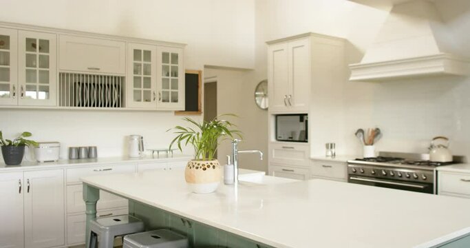 Kitchen island, sink, oven, gas stove and white furnitures in sunny kitchen