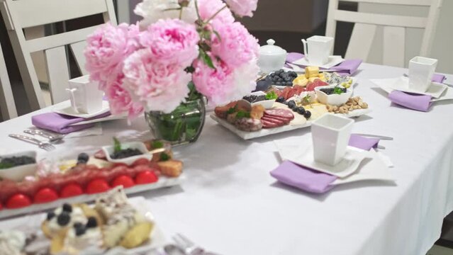 Close up shot of a sweets table set up for tea and morning snack. Pink flower centerpiece is in the middle. Purple napkins are under the plates