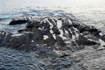 Close-up of rocky lava coast. Waves crashing on rocks