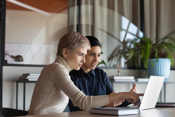 Corporate teacher showing new employee learning video at laptop, company mentor training intern. Diverse coworkers watching presentation, reading message, working together at computer