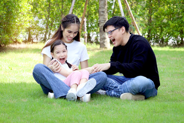 Happy family sitting on green grass, having fun and spending time together in summer garden, cute daughter girl sitting on mother lap during playing with her father at backyard. Family love bonding.