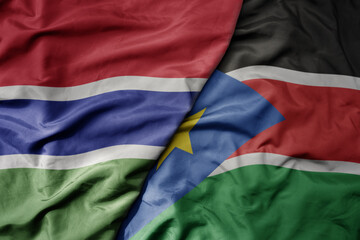 big waving national colorful flag of south sudan and national flag of gambia .