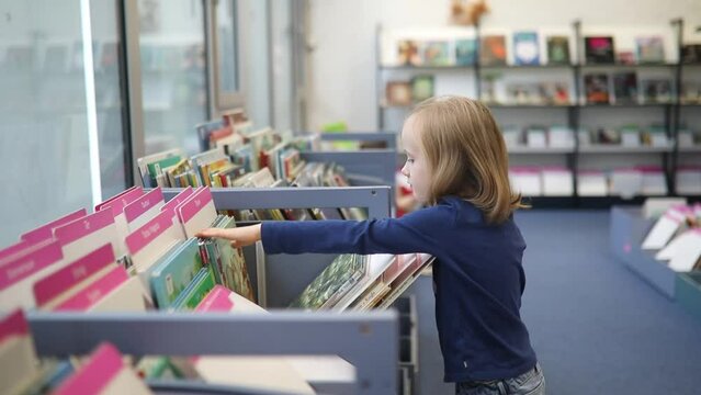 Preschooler girl selecting a book in municipal library