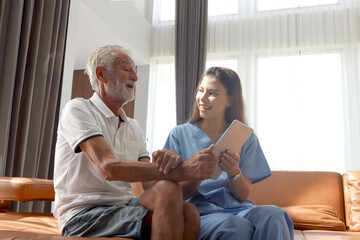 Female nurse takes care of senior patient and teaches him to use digital tablet at living room house, elderly mature grandfather learns to online internet and high-tech, nursing medical health care. - obrazy, fototapety, plakaty