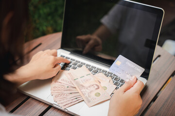 Hands of businesswoman holding thai money and credit card on laptop computer, woman using working and shopping, Online e-commerce, internet banking